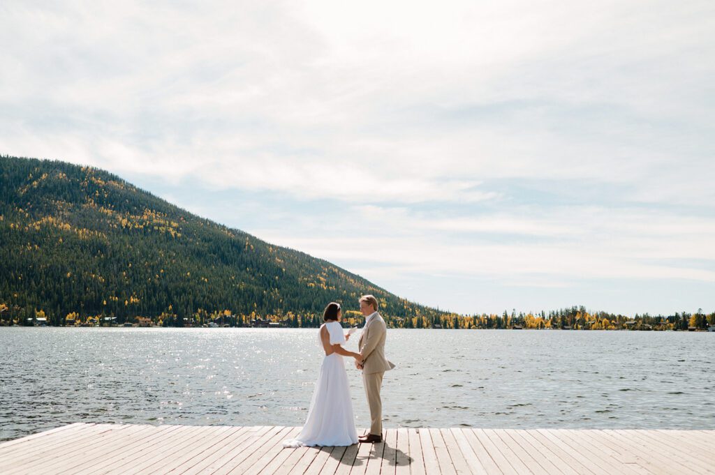 A couple standing on a dock by a mountain lake, illustrating the need to choose a wedding photographer with a proven portfolio of scenic outdoor portraits.