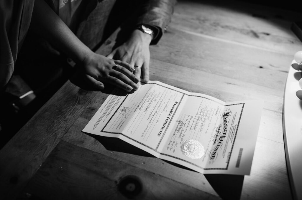 Black and white wedding detail photo of a couple signing their marriage certificate, showing meaningful moments to look for when choosing a wedding photographer.