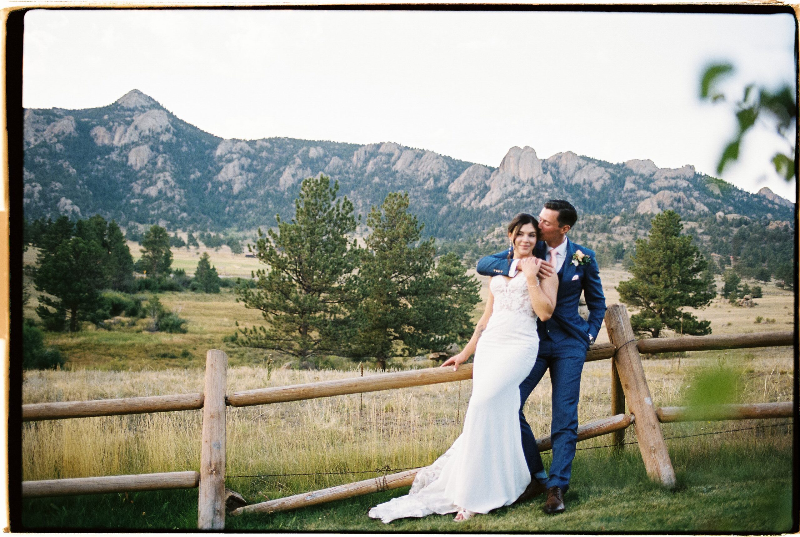 Romantic mountain wedding portrait of a couple by a wooden fence with sweeping Colorado views, capturing why late summer is often considered the best time to get married in Colorado.
