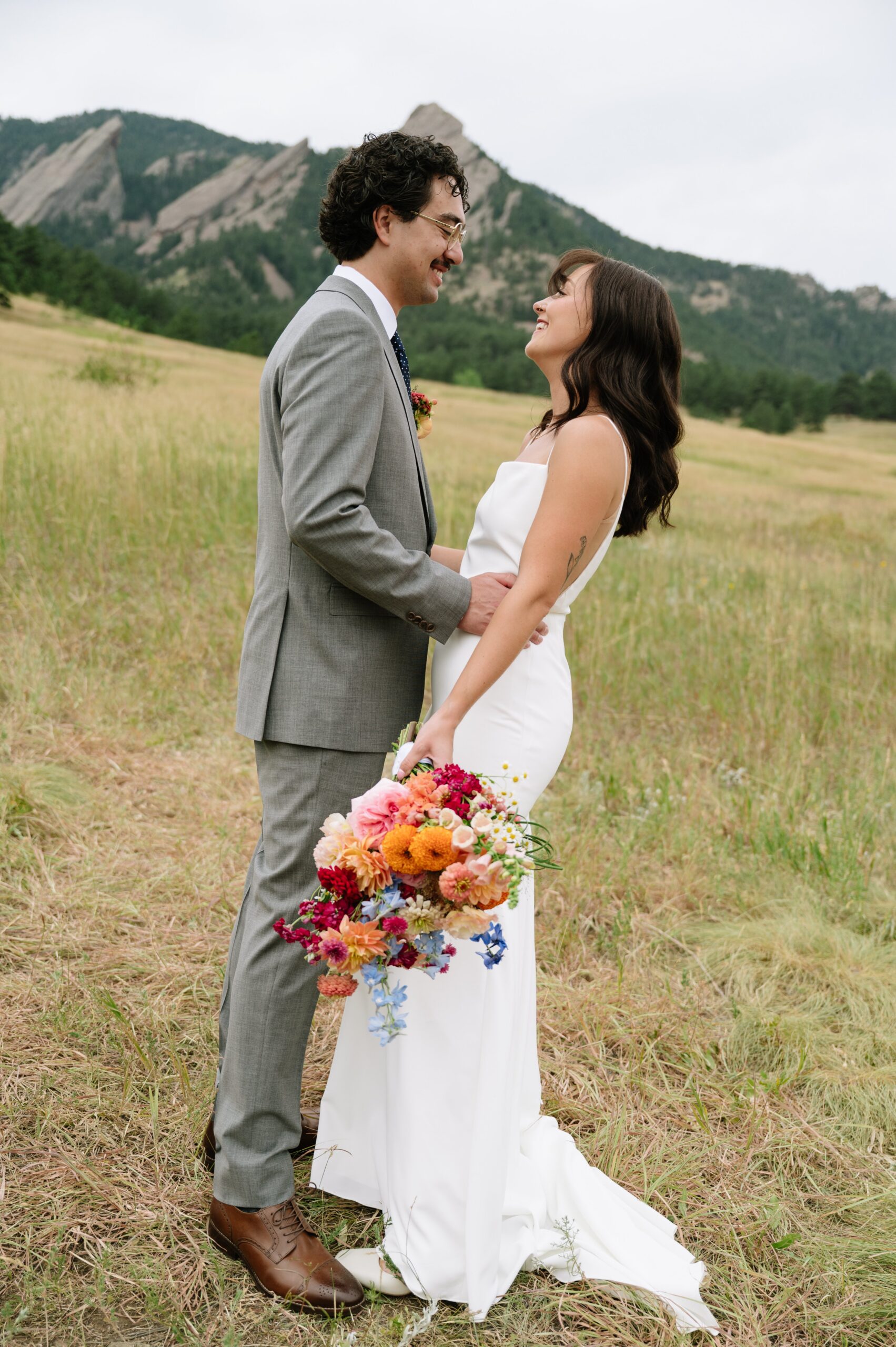 Couple smiling at each other in a mountain meadow, showcasing why summer is often the best time of year to get married in Colorado with lush greenery and mild weather.