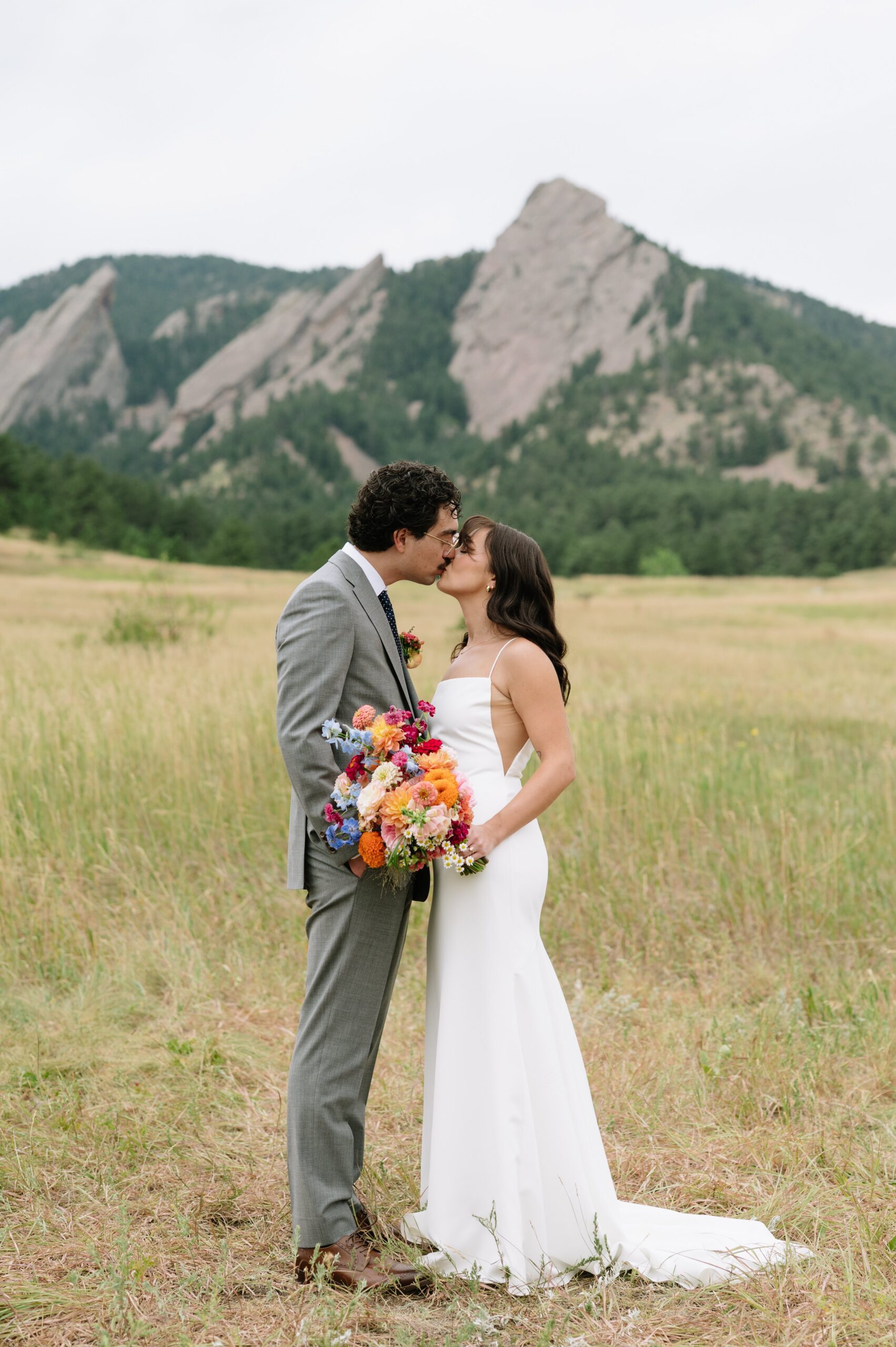 Bride and groom kissing in an open Colorado field with dramatic mountain views, highlighting one of the best months to get married in Colorado for scenic outdoor portraits.