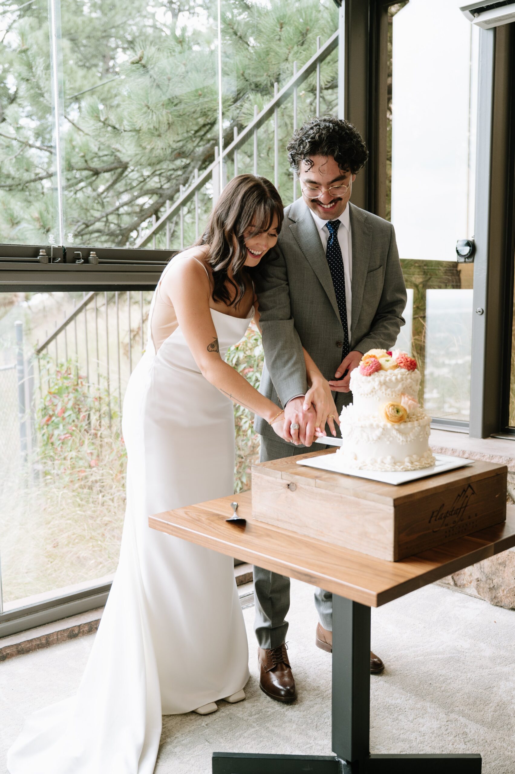 Bride and groom cutting their wedding cake indoors with mountain views, showing why summer celebrations can be the best time to get married in Colorado.