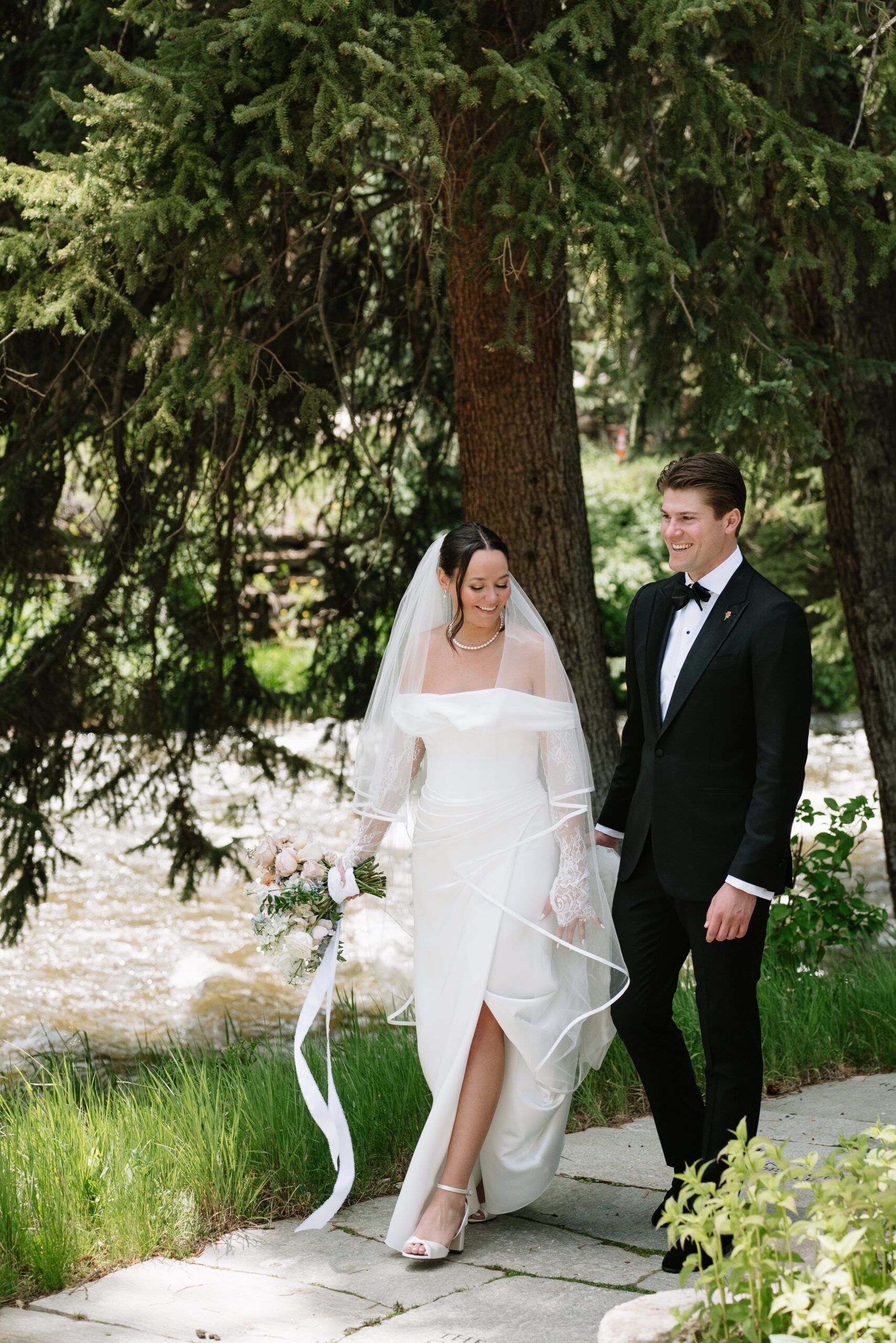 Bride and groom walking hand in hand along a riverside path, capturing a peaceful moment that shows why late spring can be the best month to get married in Colorado.