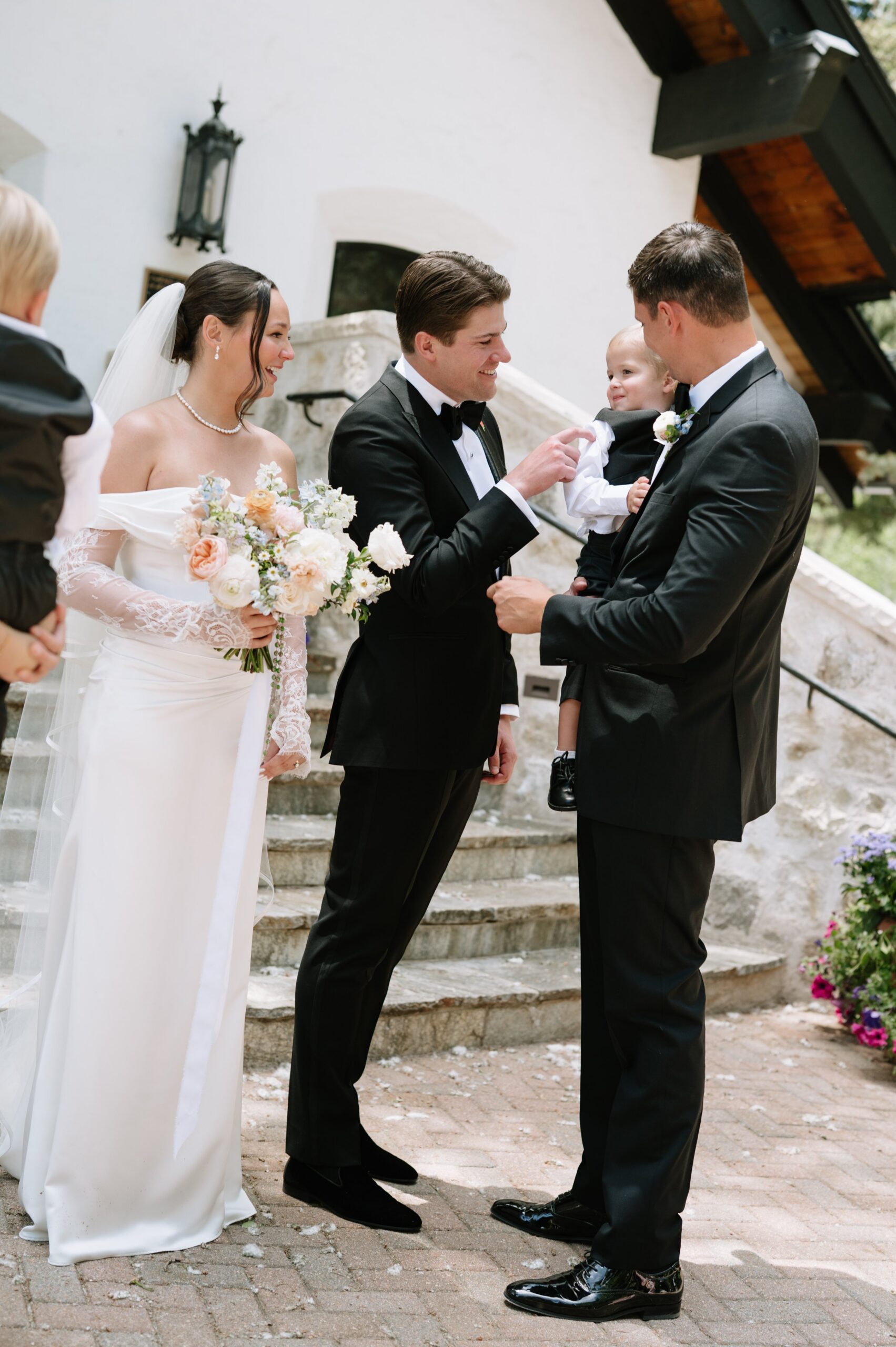 Bride and groom sharing a sweet moment with a child outside a mountain venue, illustrating why summer is often the best time to get married in Colorado for warm, family-friendly celebrations.