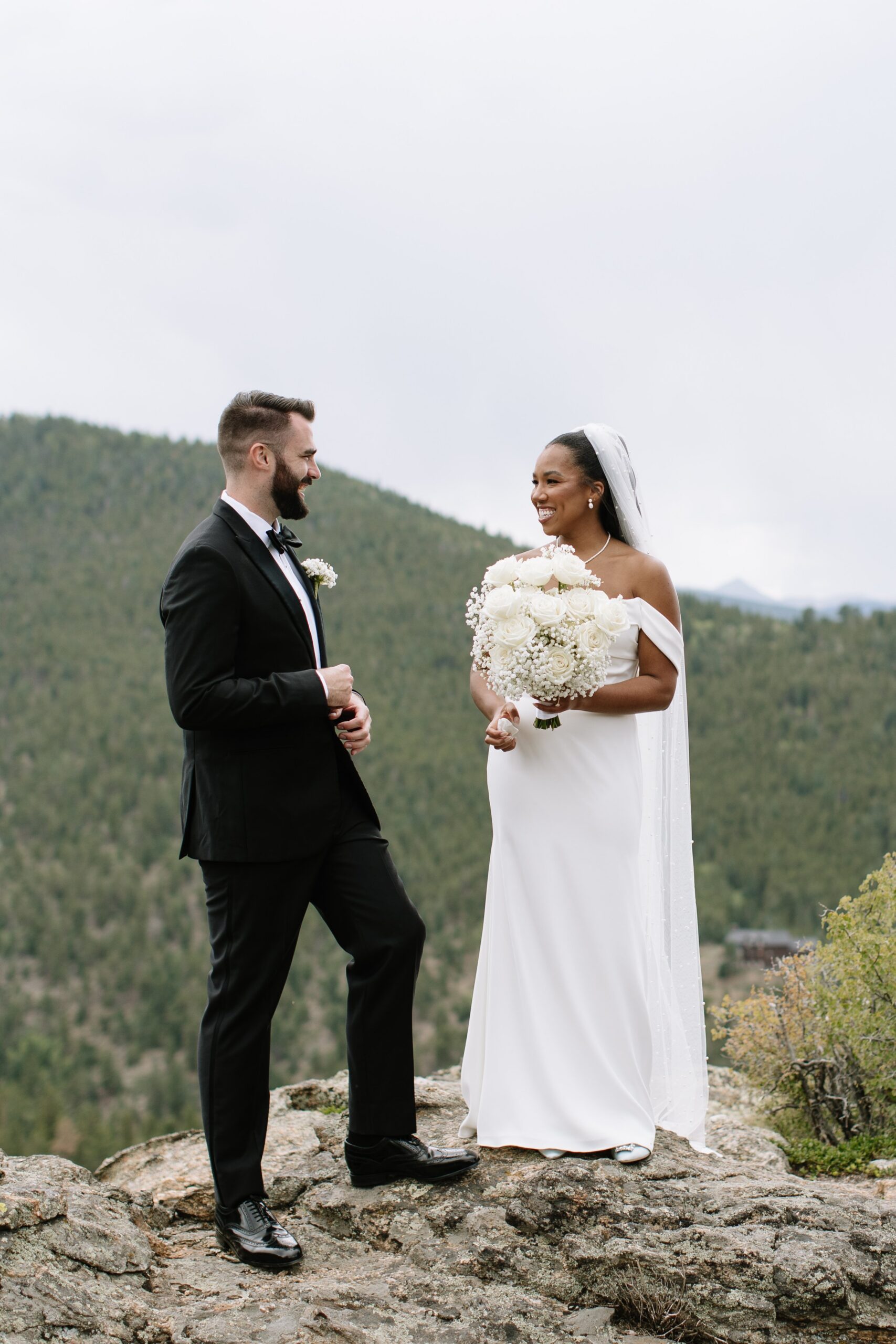 Bride and groom standing on a rocky overlook with sweeping mountain views, showcasing why summer and early fall are the best time to get married in Colorado.