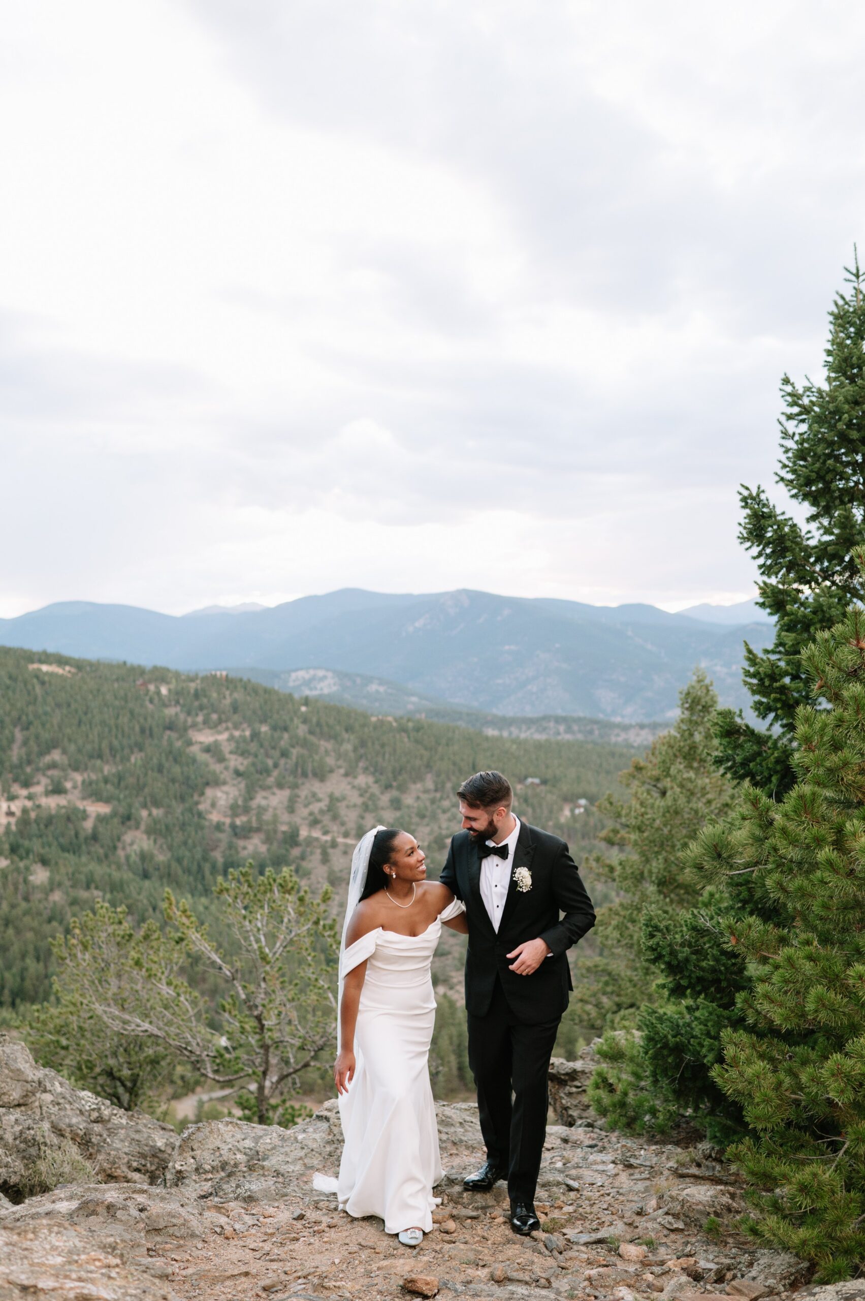 Newlyweds walking along a scenic mountain trail under soft, cloudy skies, capturing the best time of year to get married in Colorado for dramatic landscapes and comfortable weather.