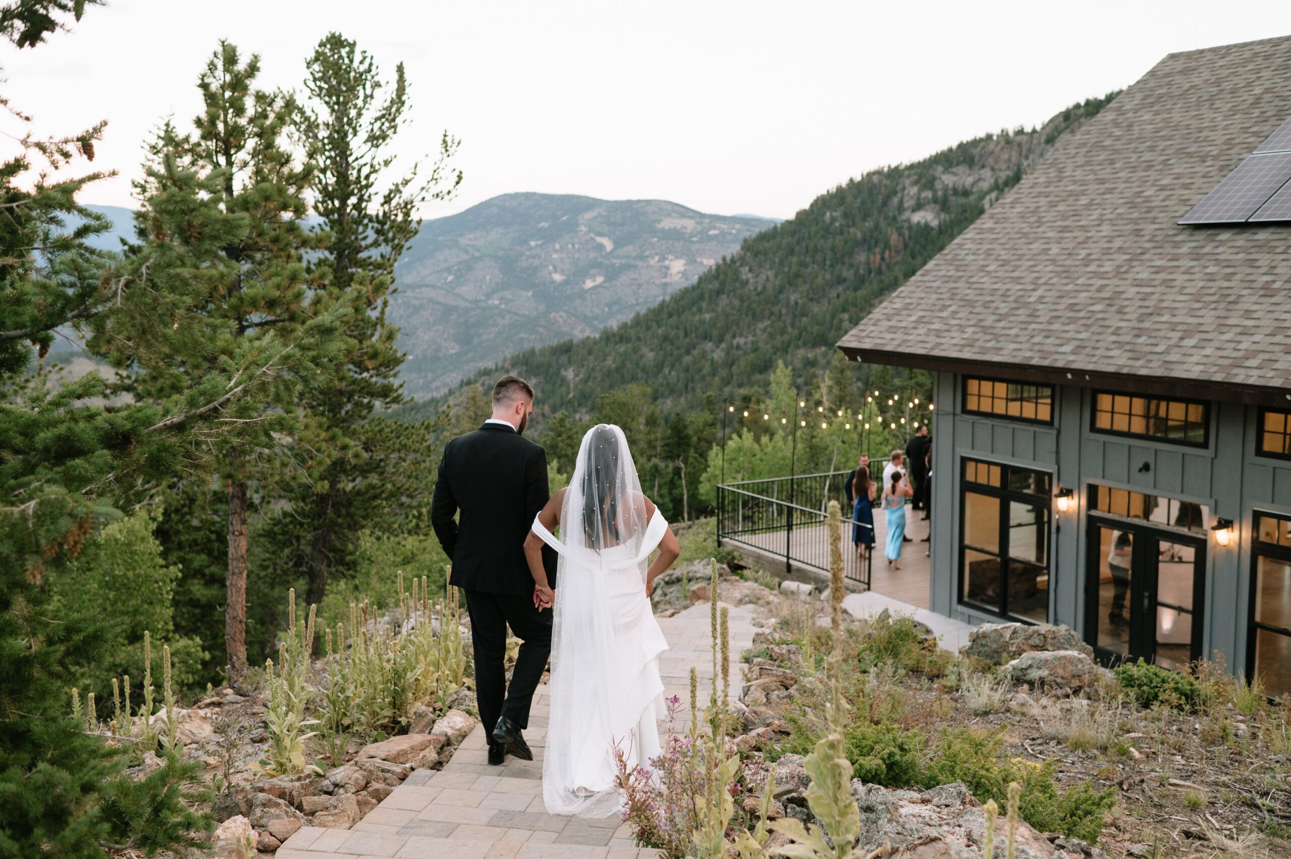 Bride and groom walking toward a mountain venue at sunset, highlighting why early evening is part of the best time to get married in Colorado for soft light and scenic views.