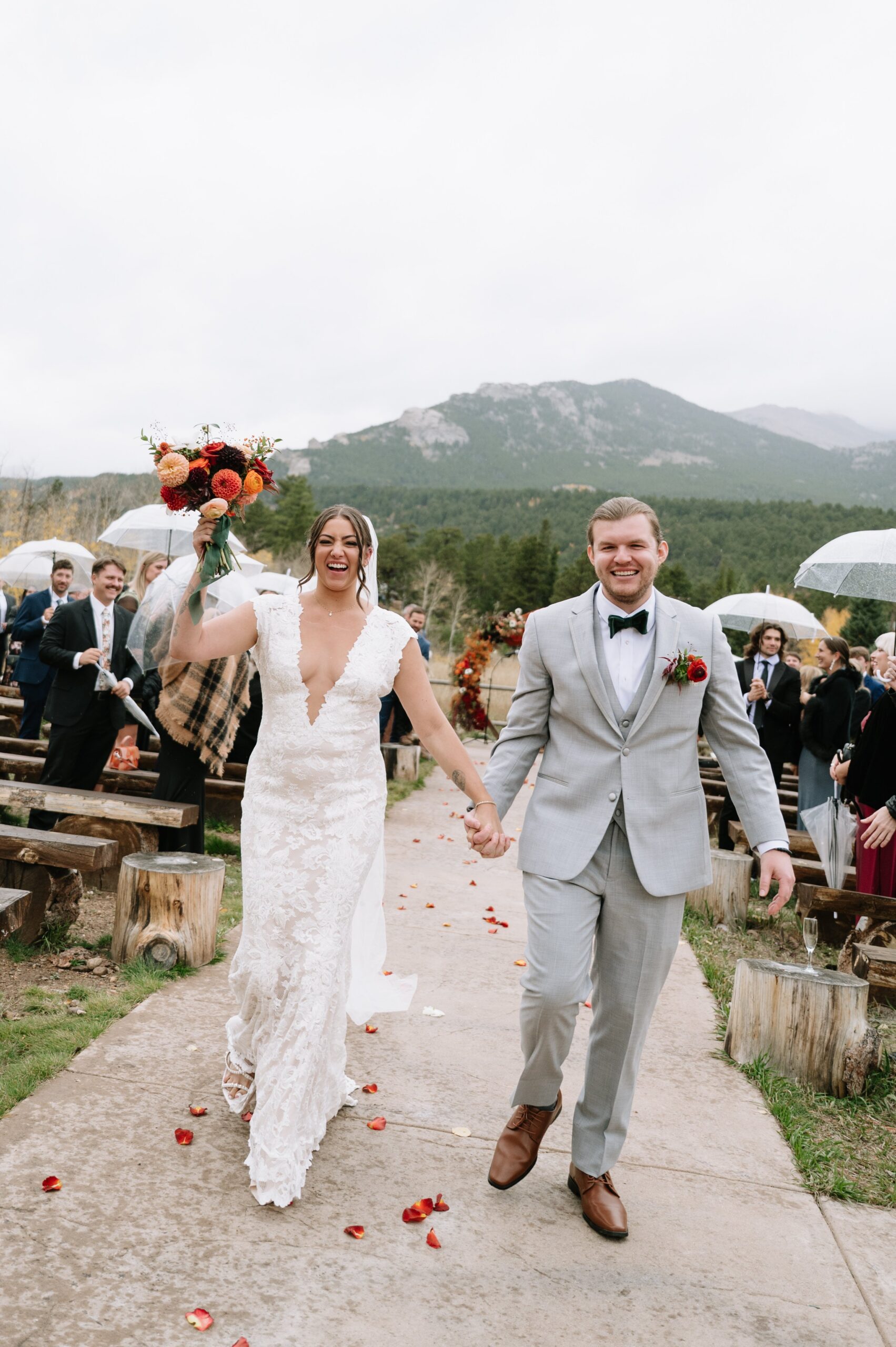 Newlyweds celebrating their recessional with guests holding umbrellas, illustrating how fall can still be the best time of year to get married in Colorado despite changing weather.