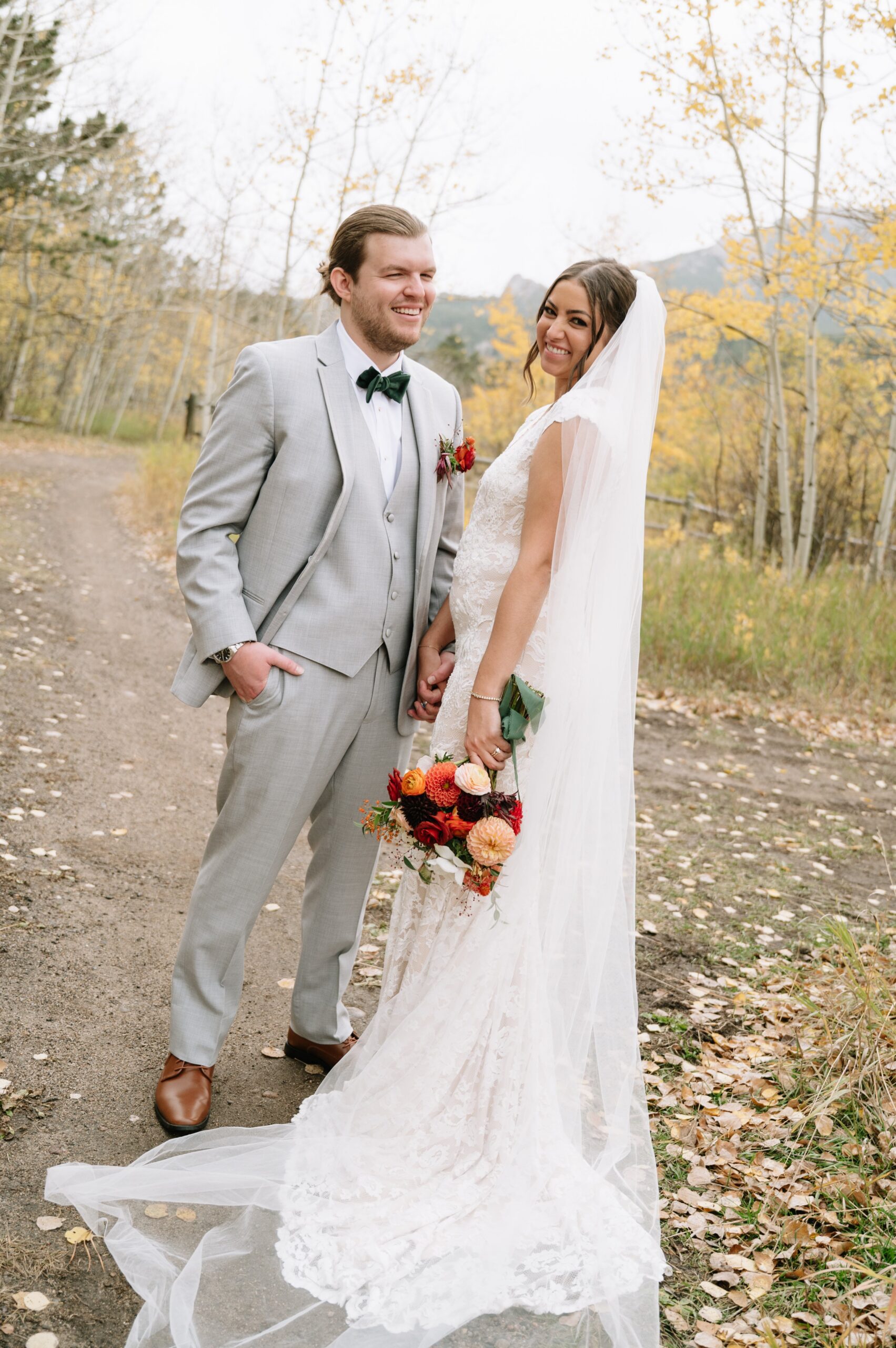 Bride and groom posing on a tree-lined path with golden leaves, capturing why autumn is considered the best month to get married in Colorado for vibrant seasonal colors.