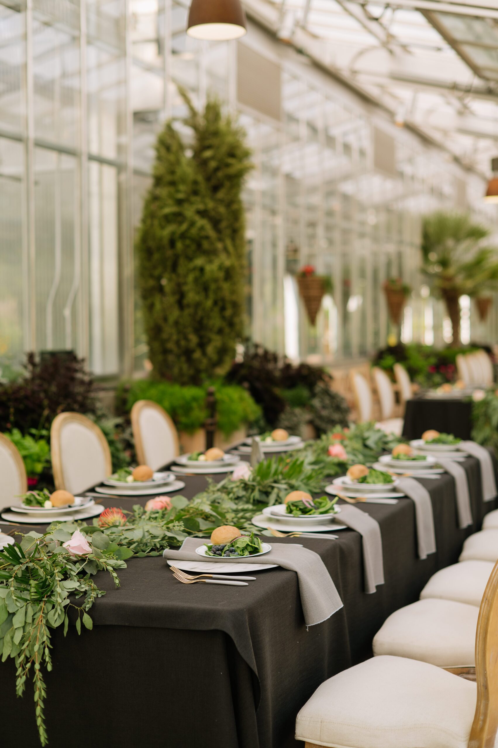 Elegant reception table setup inside a denver botanic gardens wedding venue with black linens, greenery garlands, and neatly arranged place settings.