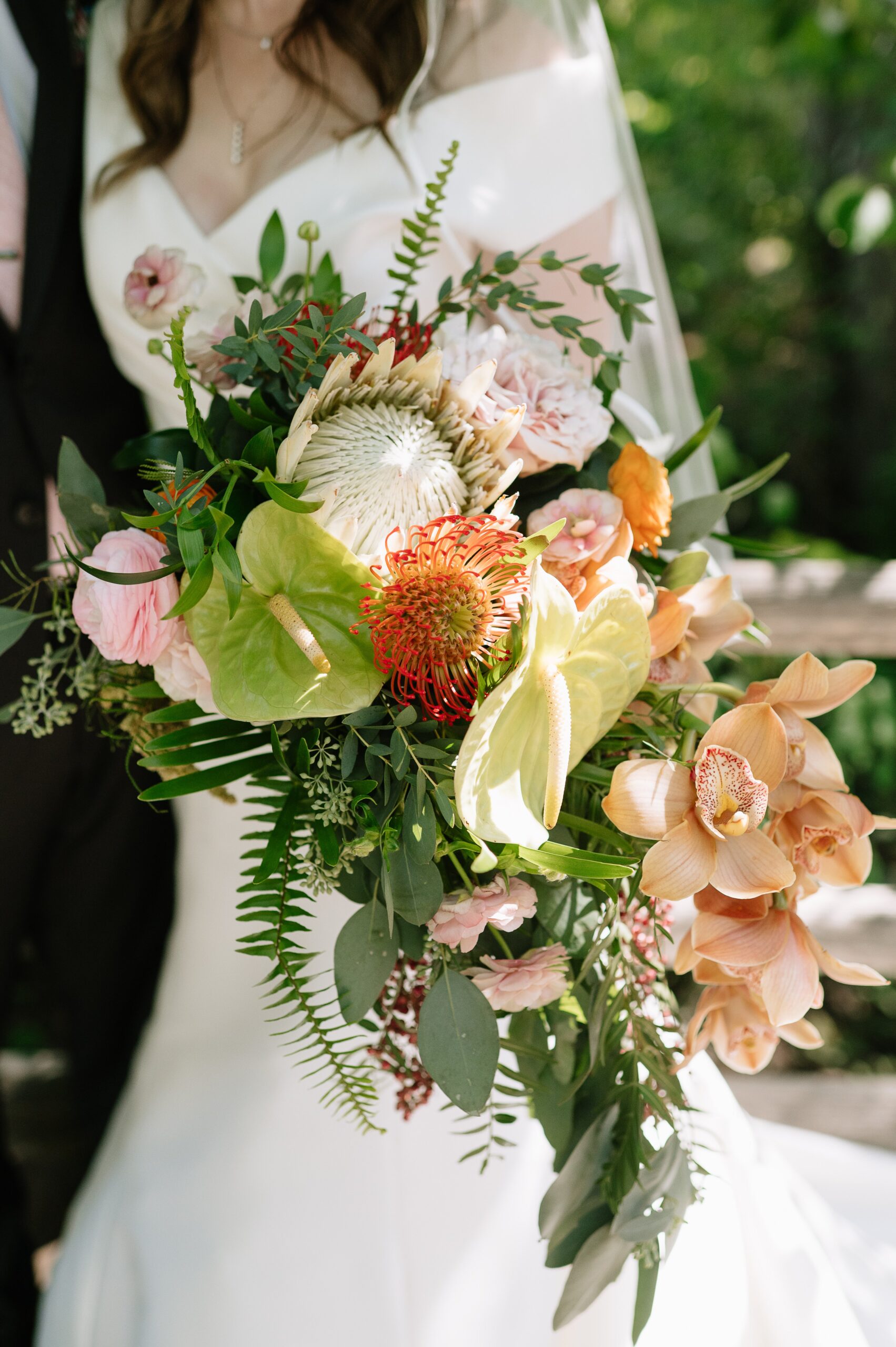 Colorful tropical bridal bouquet with orchids, anthurium, and greenery during a Denver Botanic Gardens wedding, held against a modern white gown.