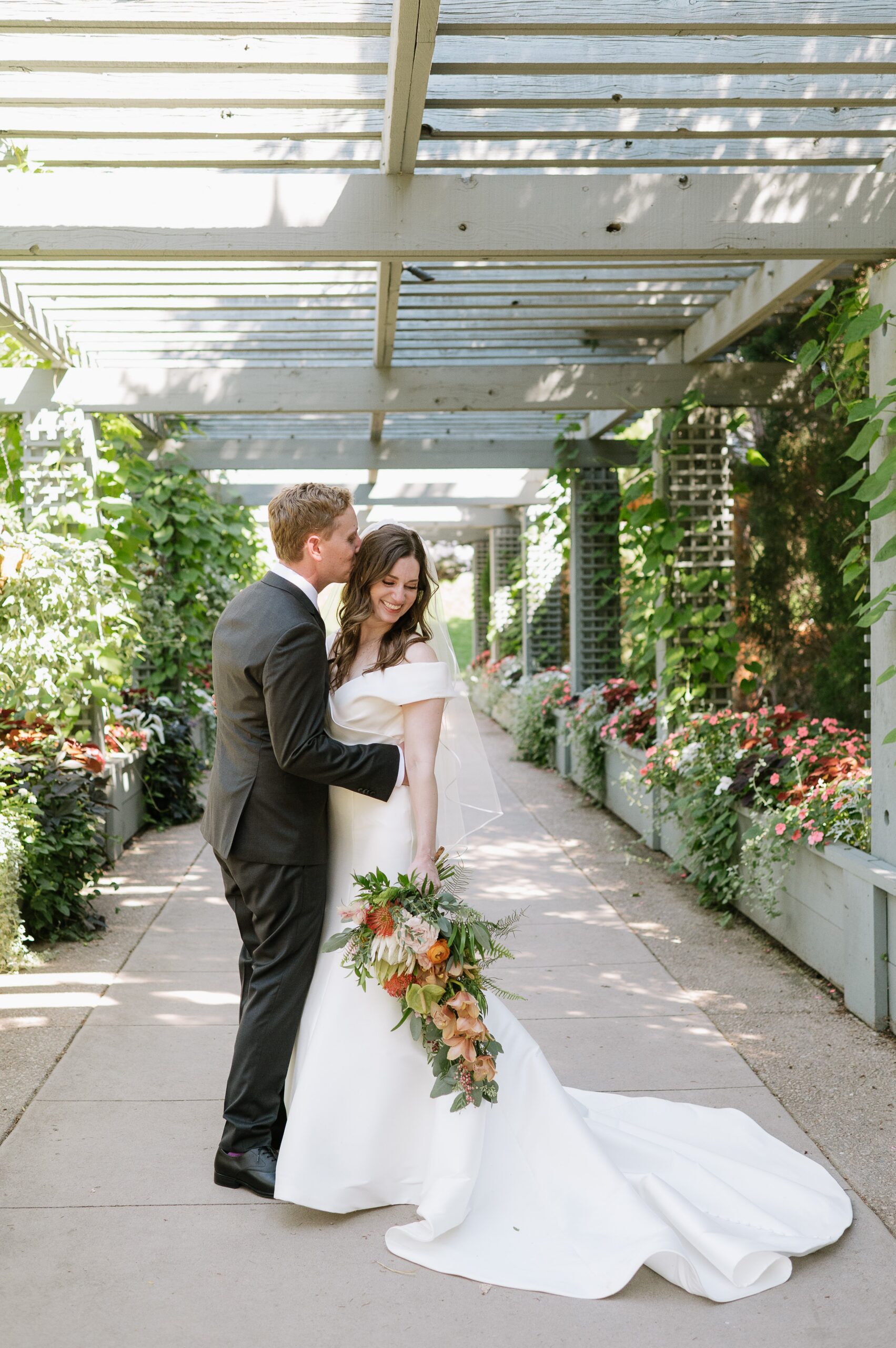Romantic portrait of the couple embracing beneath a garden pergola during a botanic gardens wedding Denver, surrounded by lush flowers and greenery.