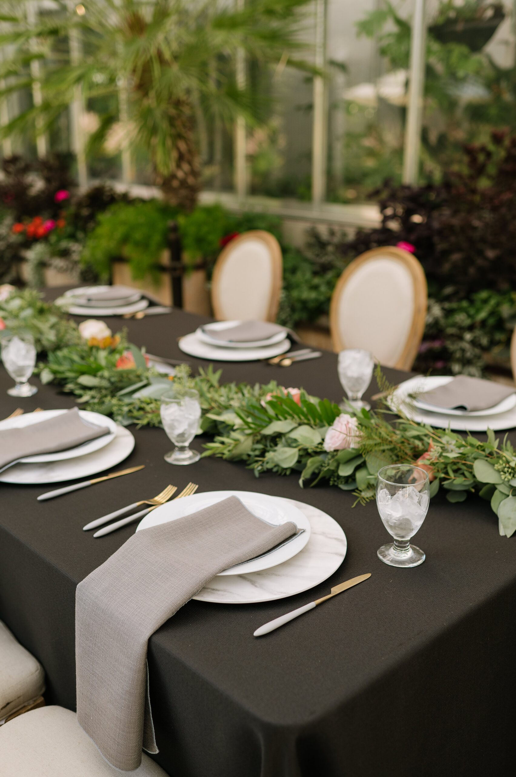 Close-up of refined table decor at a botanic gardens wedding denver with layered plates, soft linens, and greenery accents across a black tablecloth.