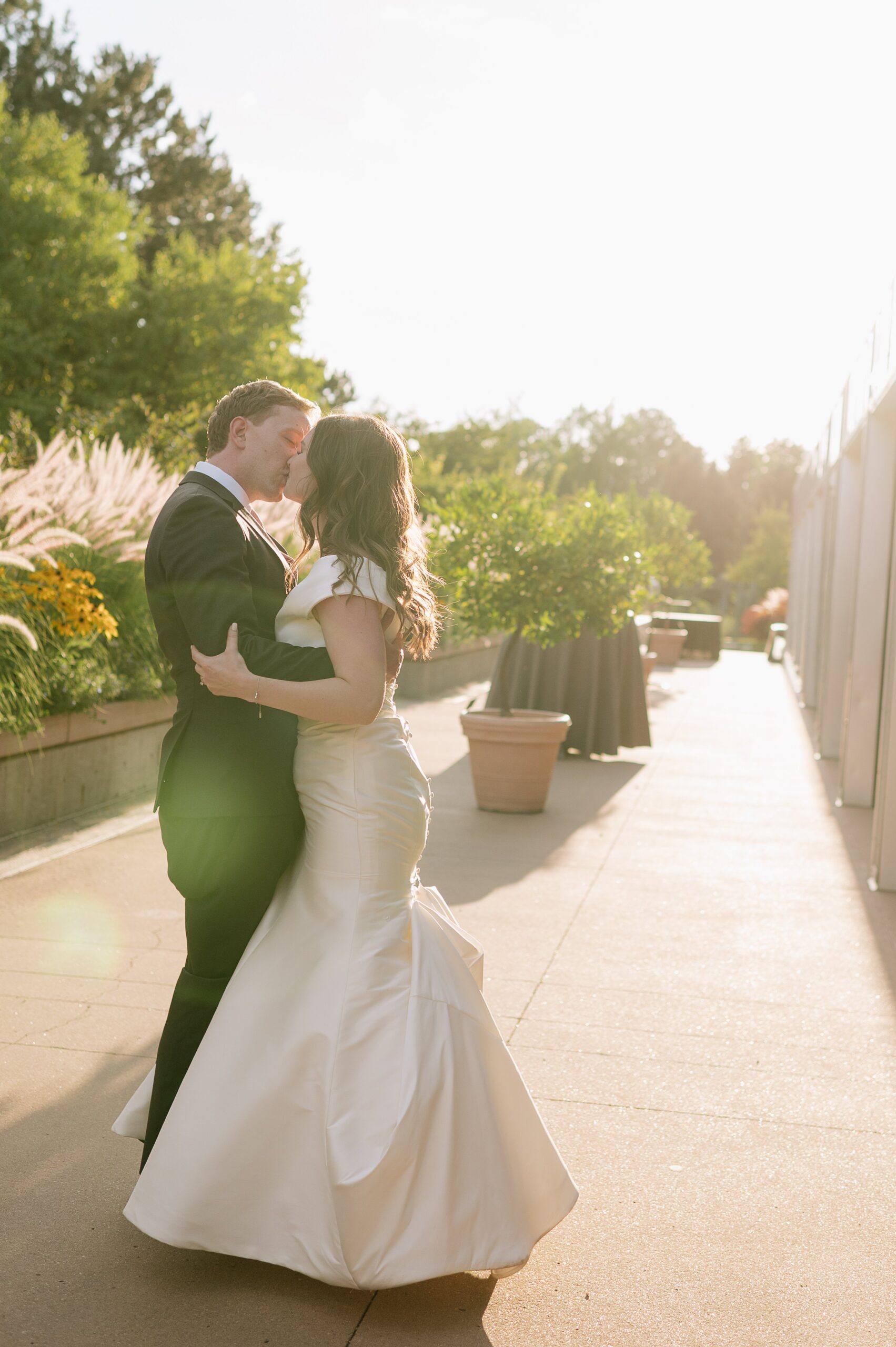 Romantic golden hour portrait of the couple kissing during a denver botanic gardens wedding, with soft sunlight and garden greenery creating a warm, glowing backdrop.