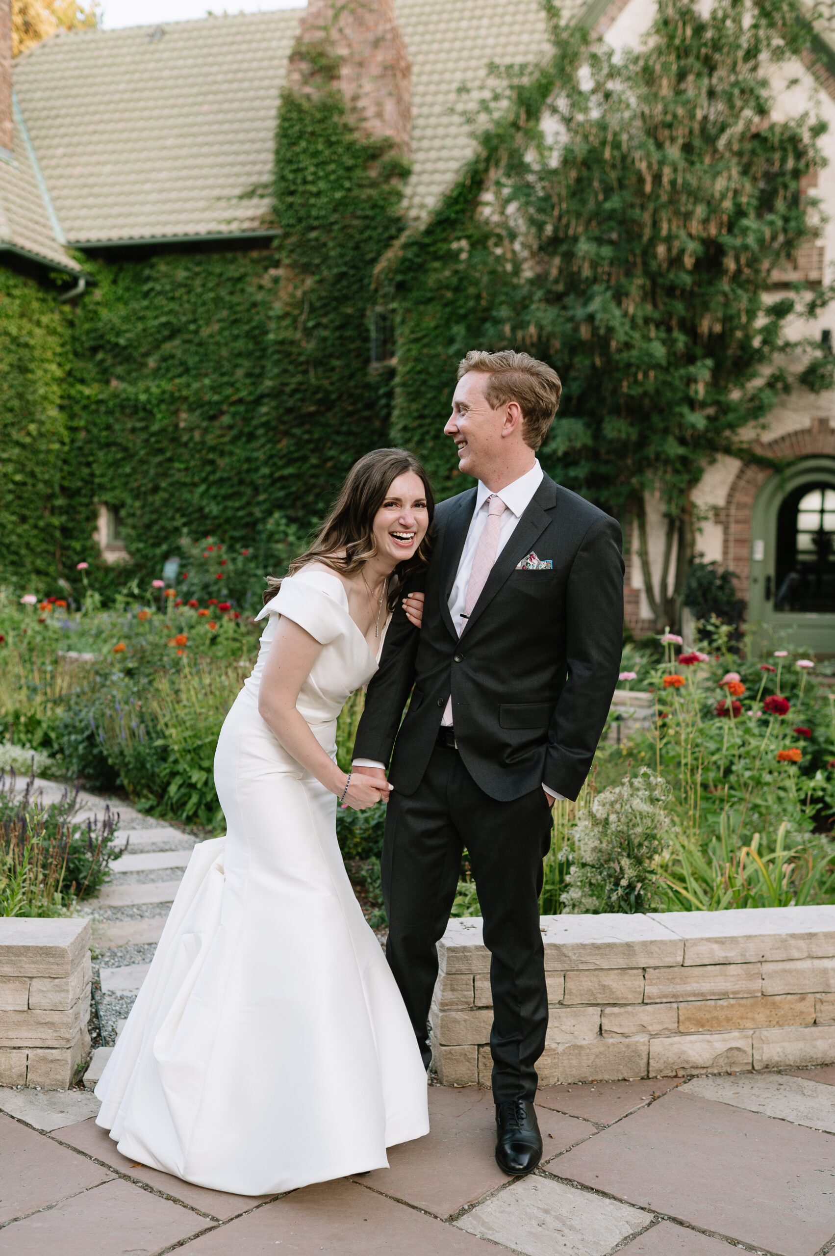Playful moment of the bride and groom laughing together during a botanic gardens denver wedding, surrounded by colorful flowers and lush greenery.