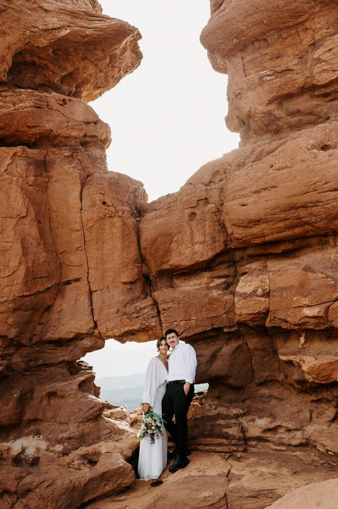 Bride and groom standing beneath red rock formations at a small outdoor wedding venue in Colorado