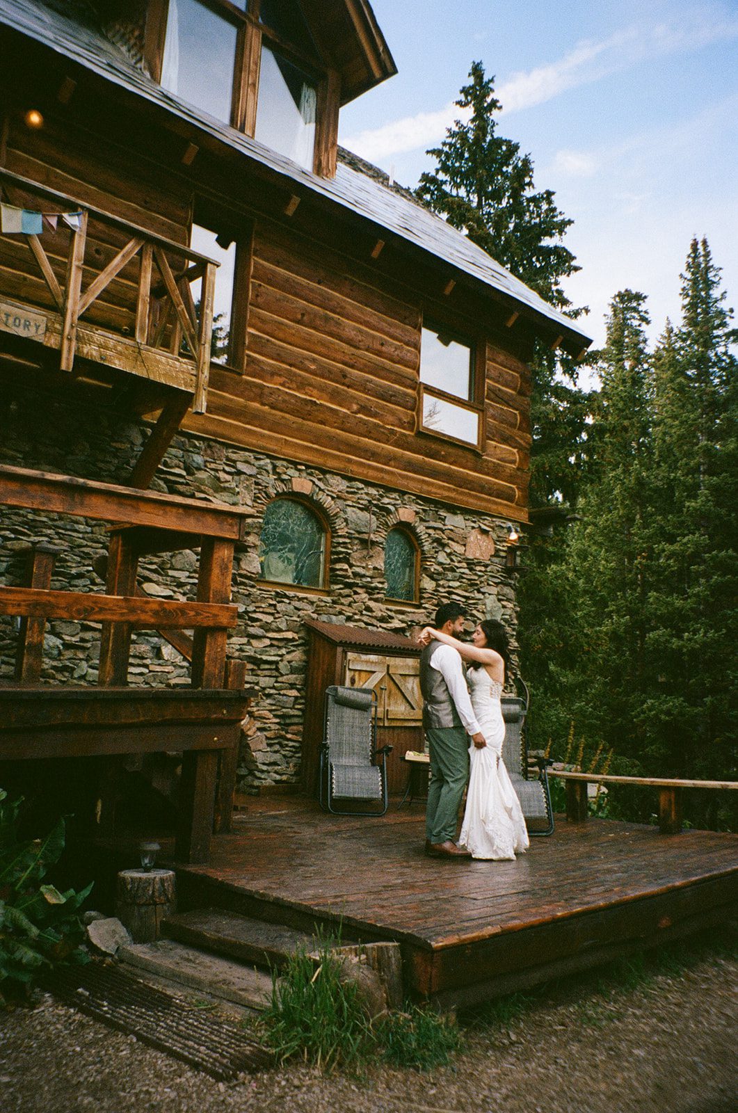Bride and groom embracing on a wooden deck outside a rustic cabin at a small wedding venue in Colorado. 