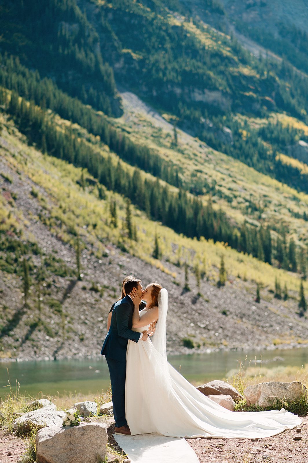 Couple sharing a kiss by a mountain lake during an intimate wedding at a small wedding venue in Colorado mountains. 