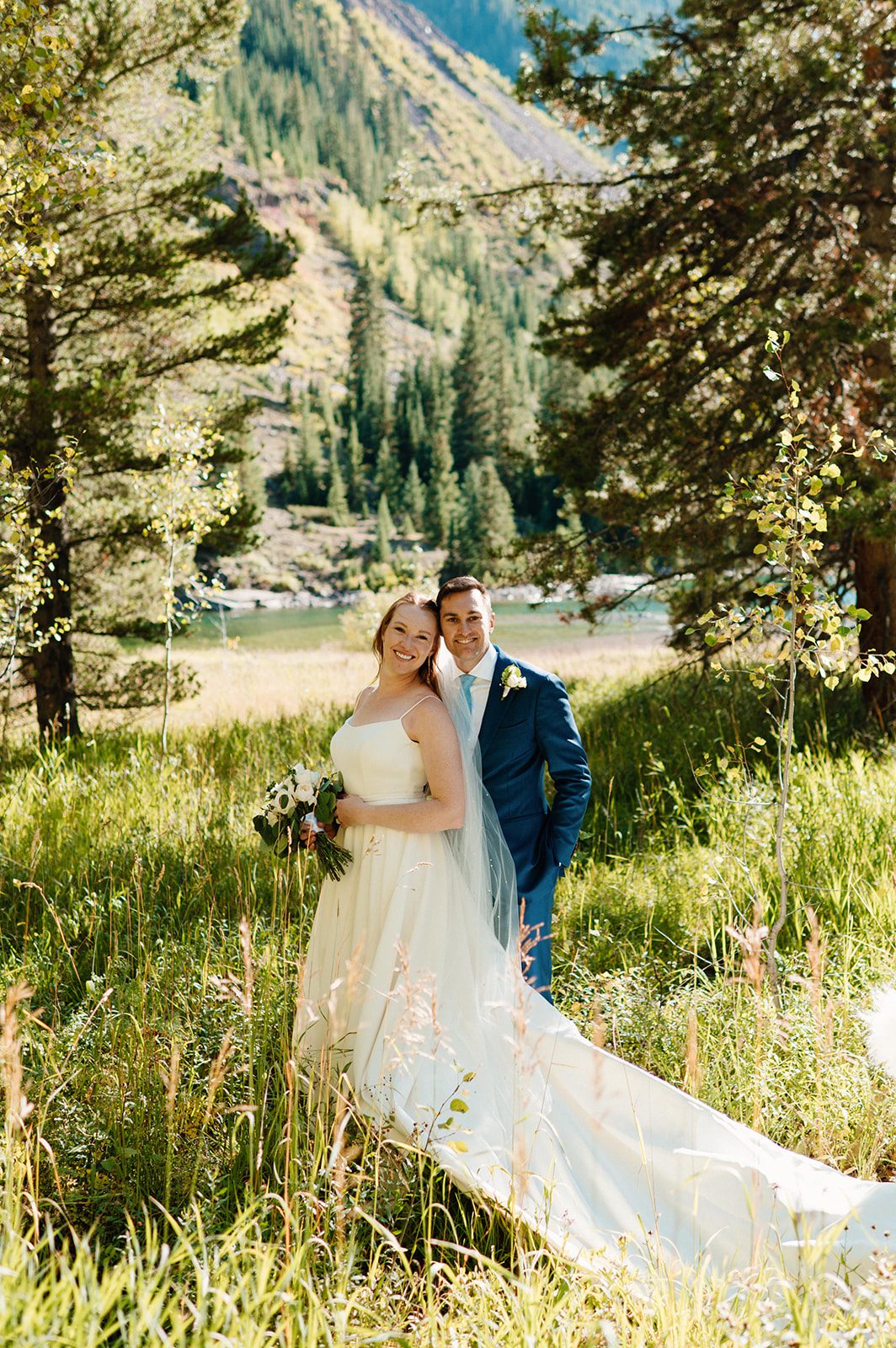 Newlyweds standing together in a sunlit mountain meadow at a small wedding venue in Colorado mountains. 