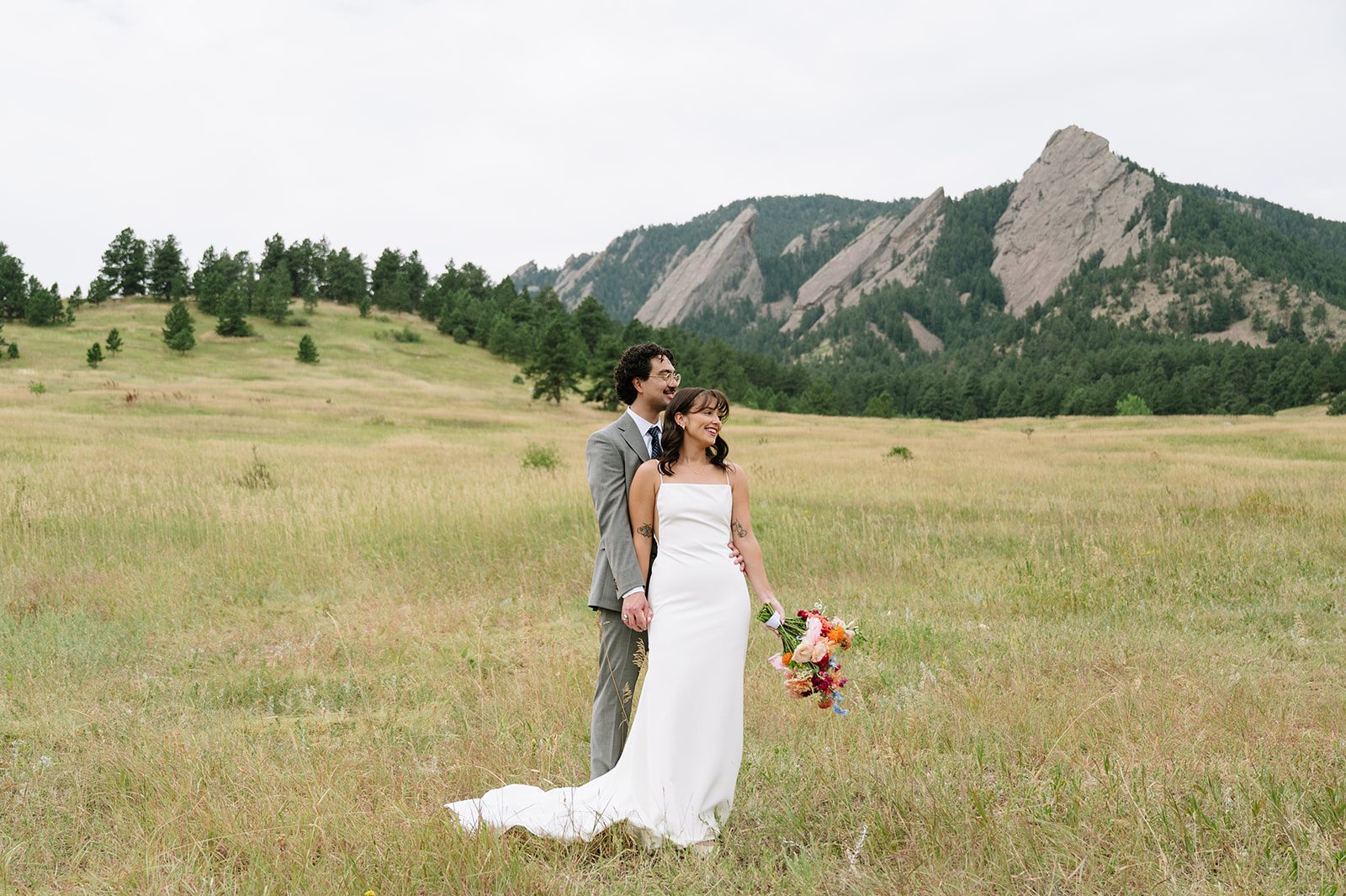 Couple standing in an open field with the Flatirons behind them at a small wedding venue in Colorado with mountain views. 