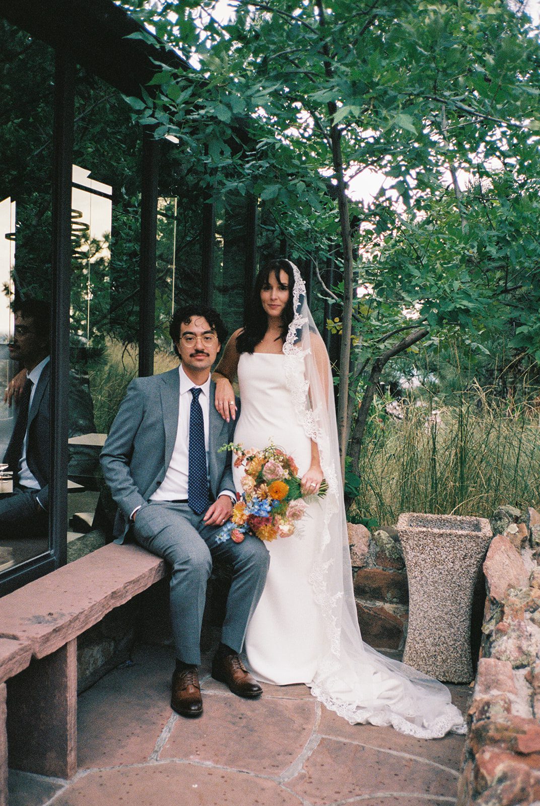 Bride and groom posing beside a glass windows surrounded by greenery at a small wedding venue in Colorado with mountain views. 