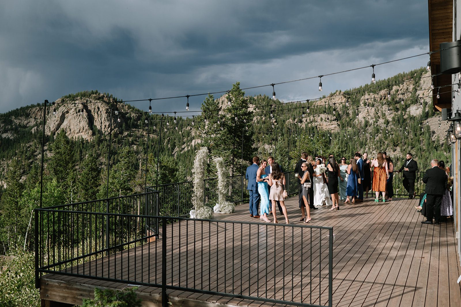 candid photo of wedding guests mingling on a wooden deck with a mountain backdrop at a north star gatherings wedding