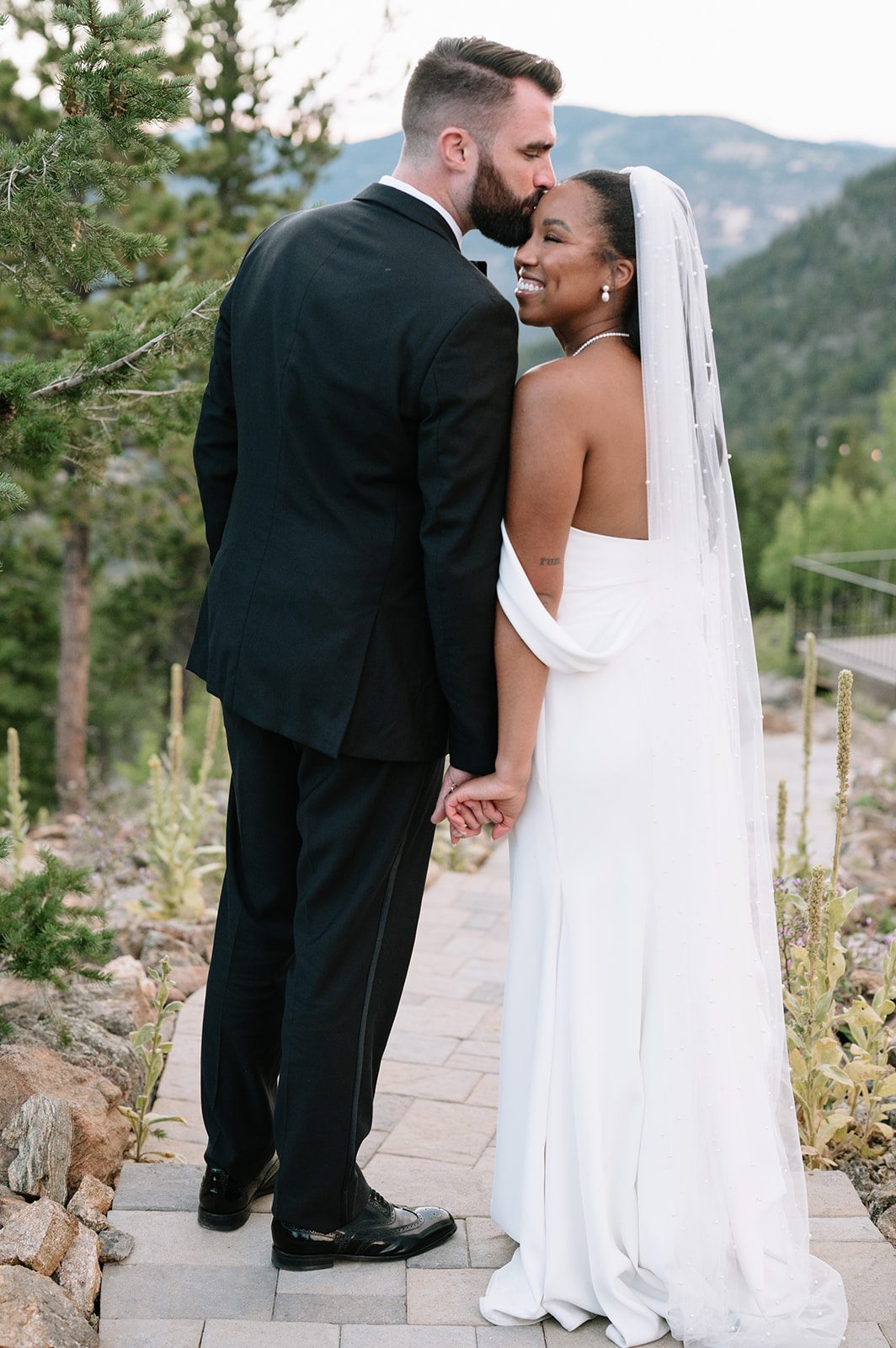 groom kissing his bride on the forehead while she smiles during their north star gatherings photoshoot