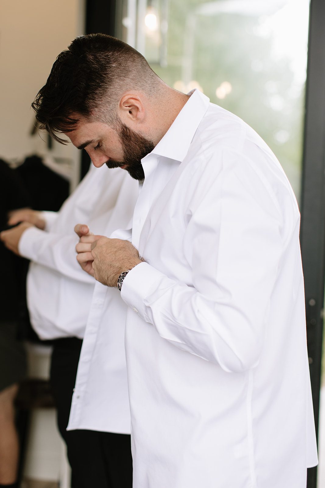 groom buttoning his whote shirt while getting ready for his ​north star gatherings idaho springs co wedding