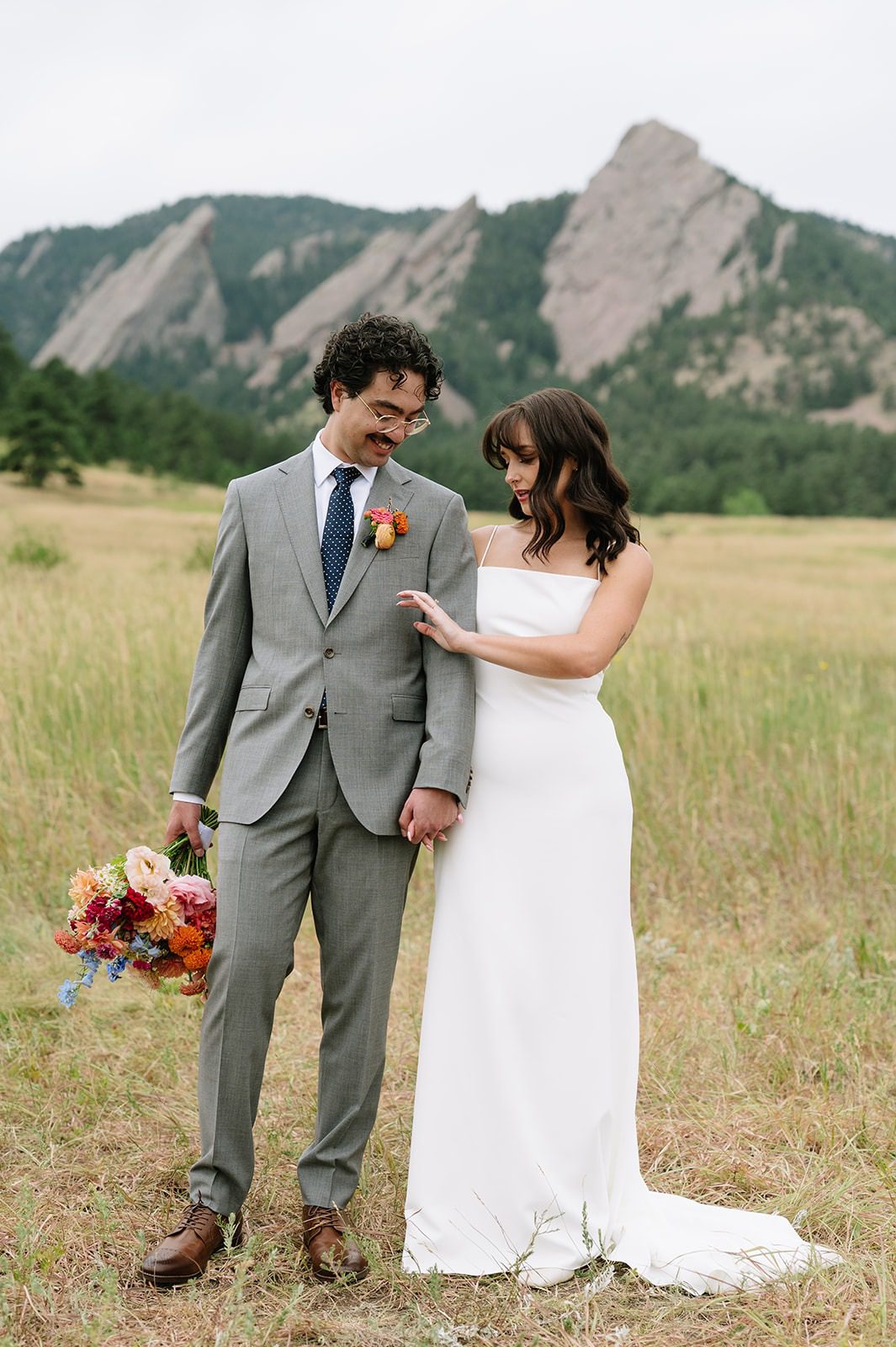 Bride and groom look at ther wedding ring in a Chautauqua Park meadow with the Boulder Flatirons behind them.