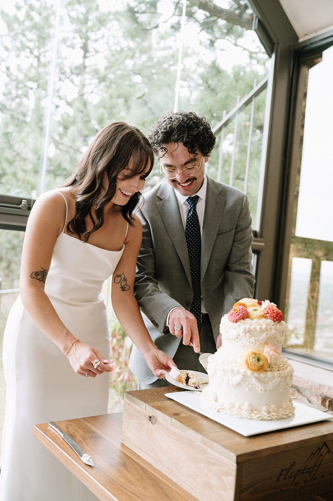 Bride and groom smile while cutting a two-tier wedding cake decorated with colorful flowers at Flagstaff House Restaurant.